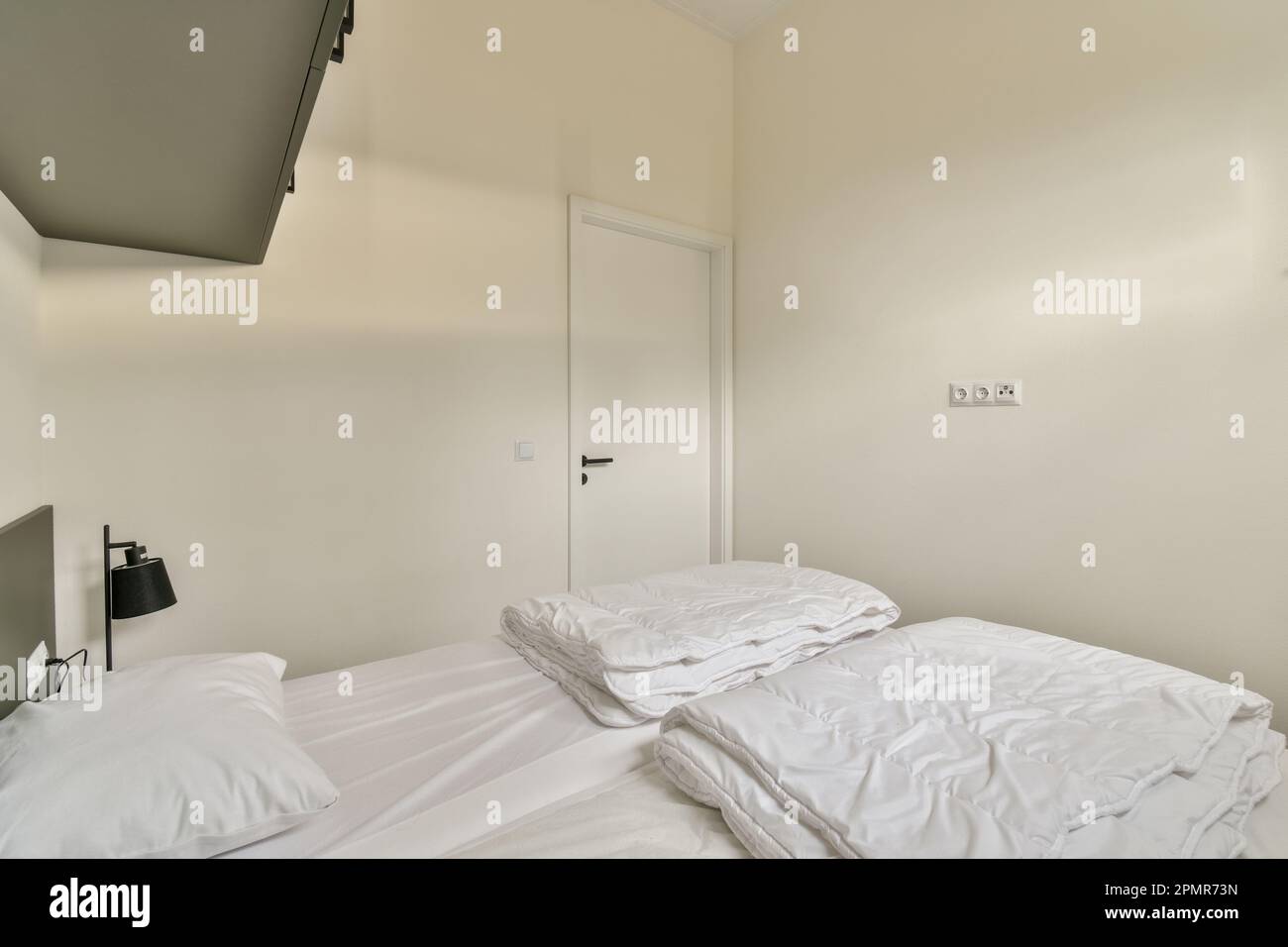 un lit avec des draps blancs et un écran plat monté au-dessus de la tête de lit en face du lit Banque D'Images