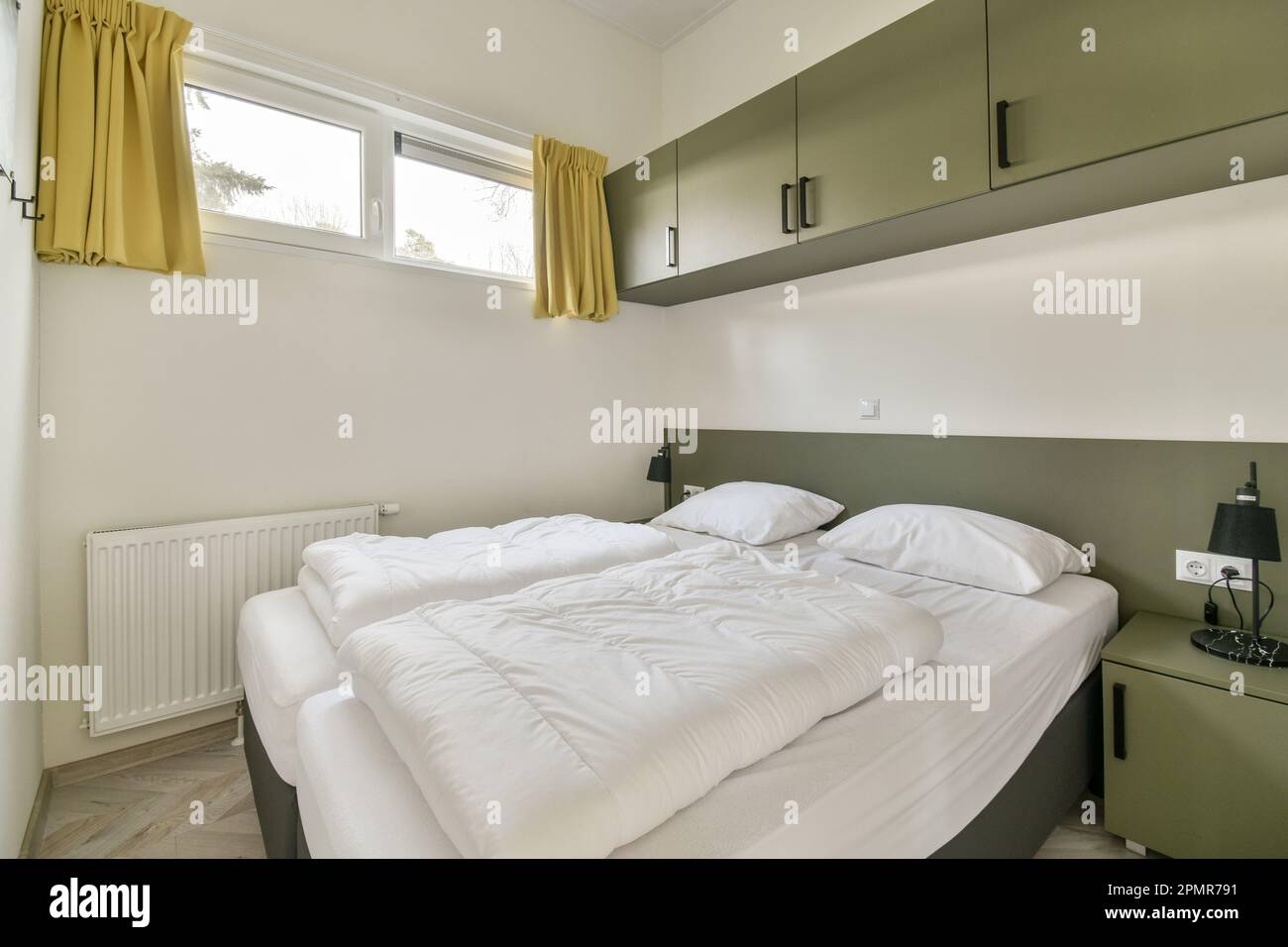 un lit avec des draps blancs et des rideaux jaunes sur la tête de lit est à côté d'une fenêtre de cabinetd verte Banque D'Images