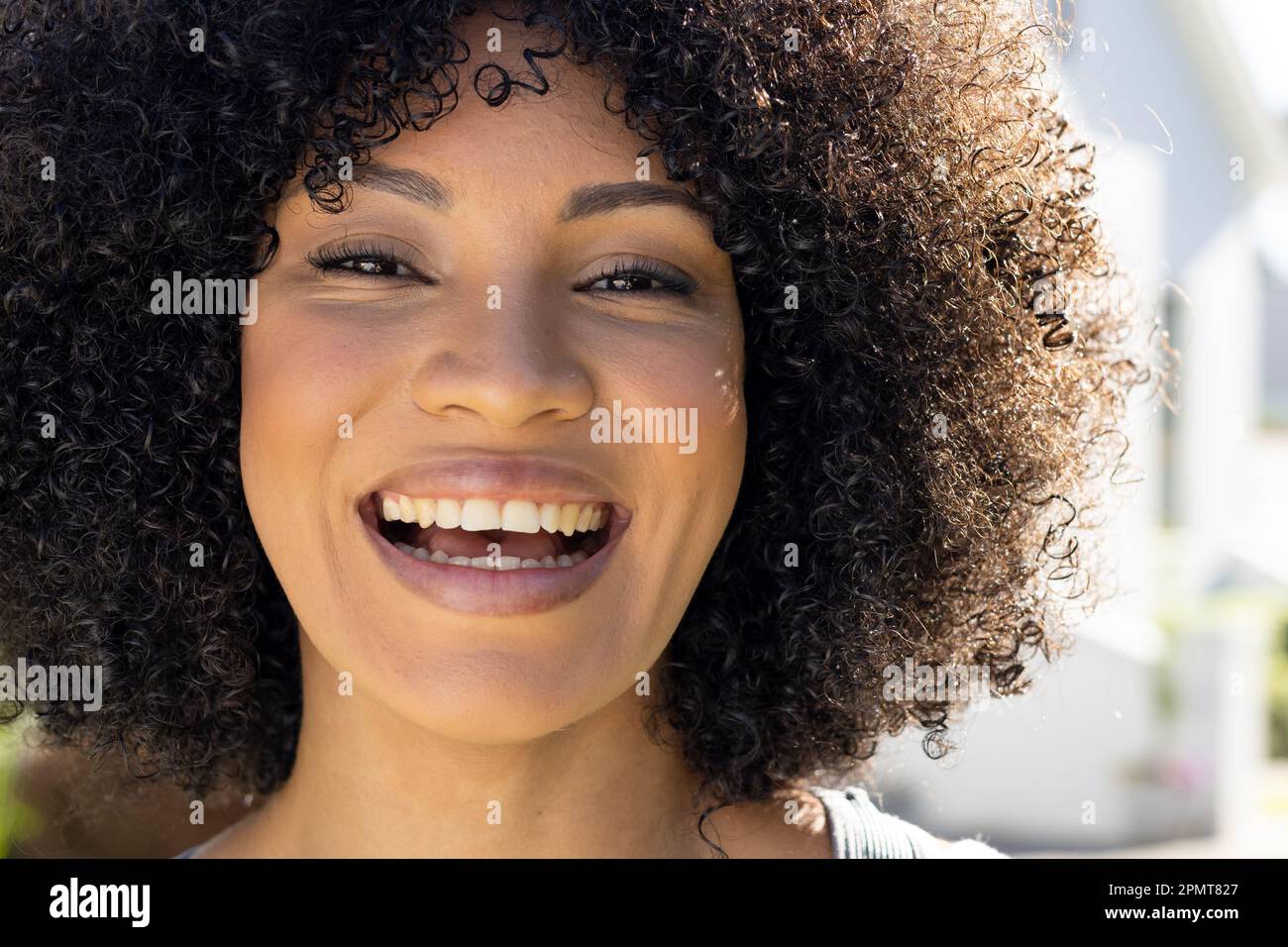 Portrait d'une heureuse femme biraciale riant et regardant l'appareil photo dans un jardin ensoleillé Banque D'Images