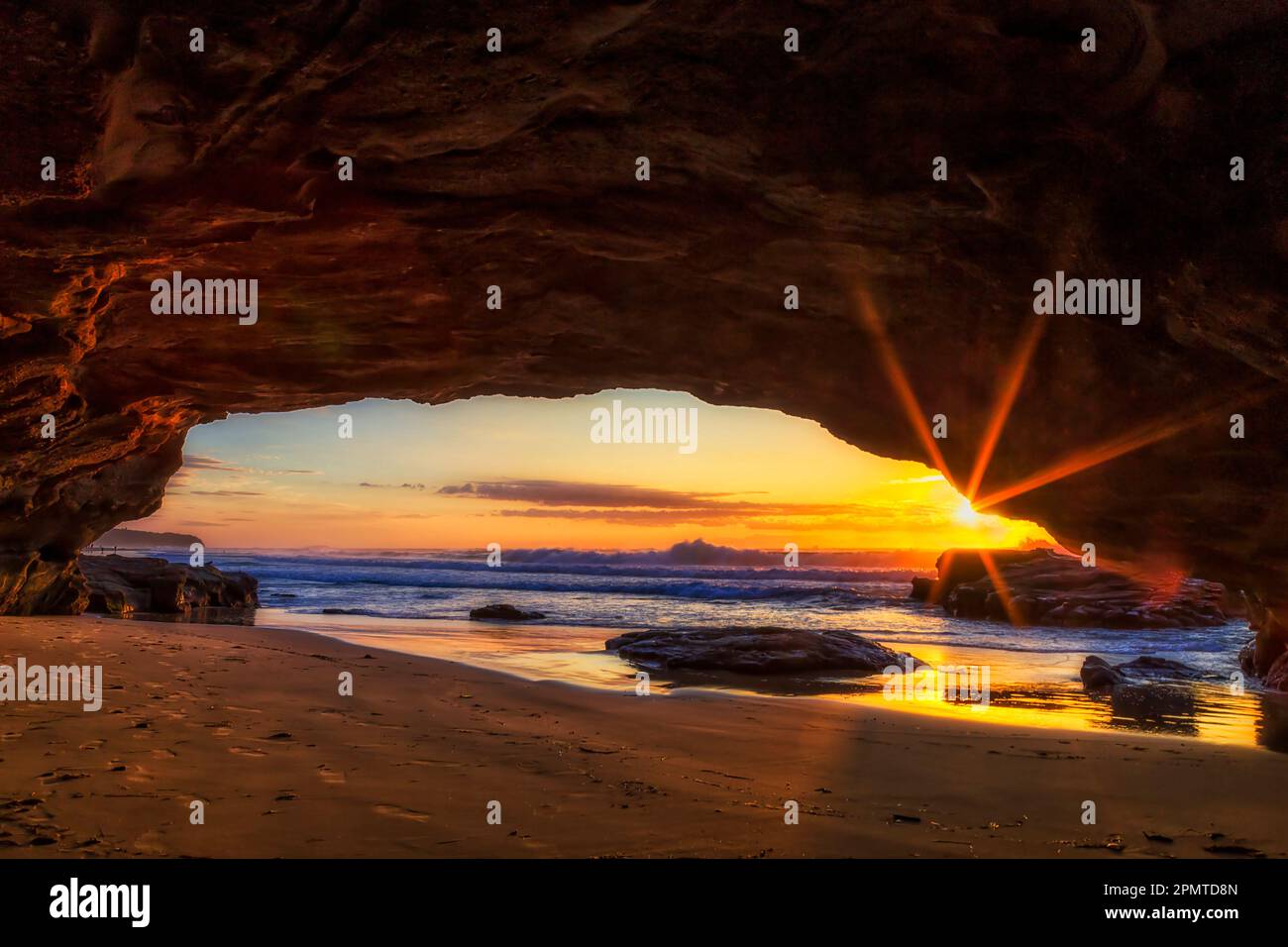 Soleil raies du soleil levant sur l'horizon de l'océan Pacifique depuis l'intérieur de la grotte de grès de la plage de Caves. Banque D'Images