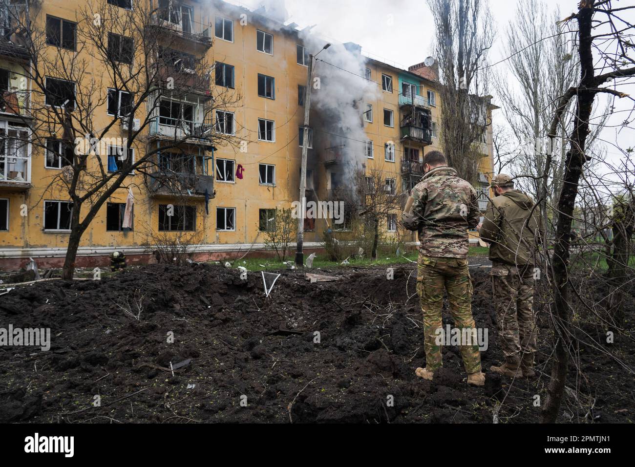 Sloviansk, Ukraine. 14th avril 2023. Les soldats se tiennent à côté de la dent créée par la fusée tandis qu'un bâtiment résidentiel brûle en arrière-plan à Sloviansk. Les troupes russes ont attaqué la ville ukrainienne orientale Sloviansk le grand vendredi de l'est orthodoxe. Les autorités ont déclaré qu'il s'agit de la plus grosse attaque à la roquette depuis des mois, causant au moins 8 morts et 21 blessés, dont des enfants et de nombreux bâtiments détruits. Le responsable a également déclaré qu'au moins 7 missiles avaient été tirés au cours de l'après-midi de vendredi. Crédit : SOPA Images Limited/Alamy Live News Banque D'Images