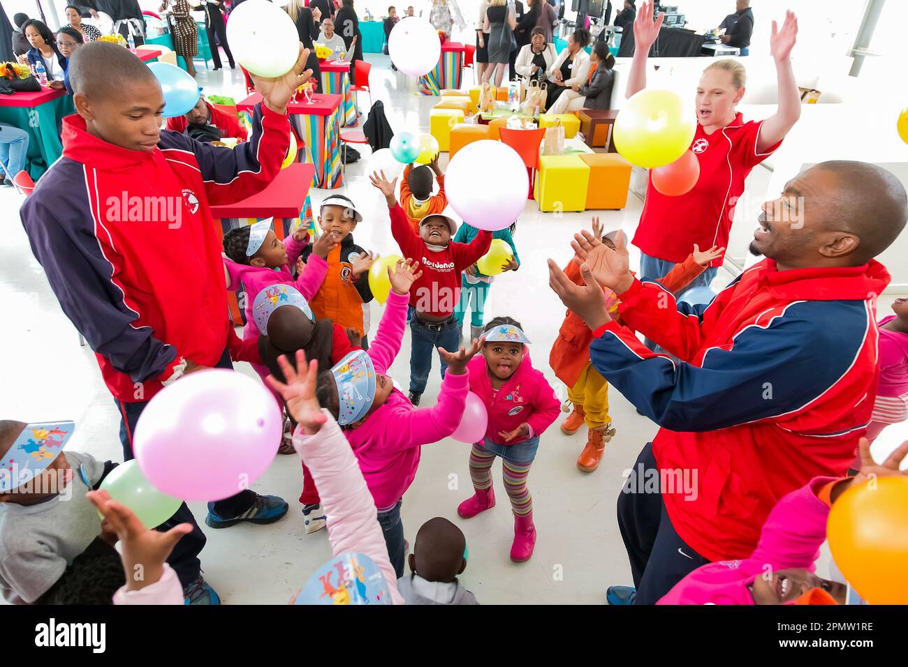Un groupe joyeux d'adultes et d'enfants jouant ensemble dans un cercle, chacun tenant des ballons colorés remplis d'hélium dans leurs mains Banque D'Images