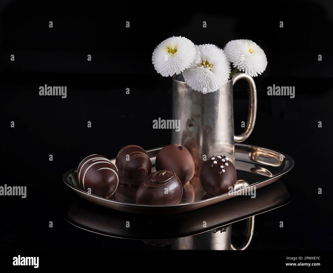 Chocolats précieux magnifiquement disposés sur un plateau argenté, vase fleuri vintage décoré en argent avec un bouquet de fleurs de Marguerite. Banque D'Images