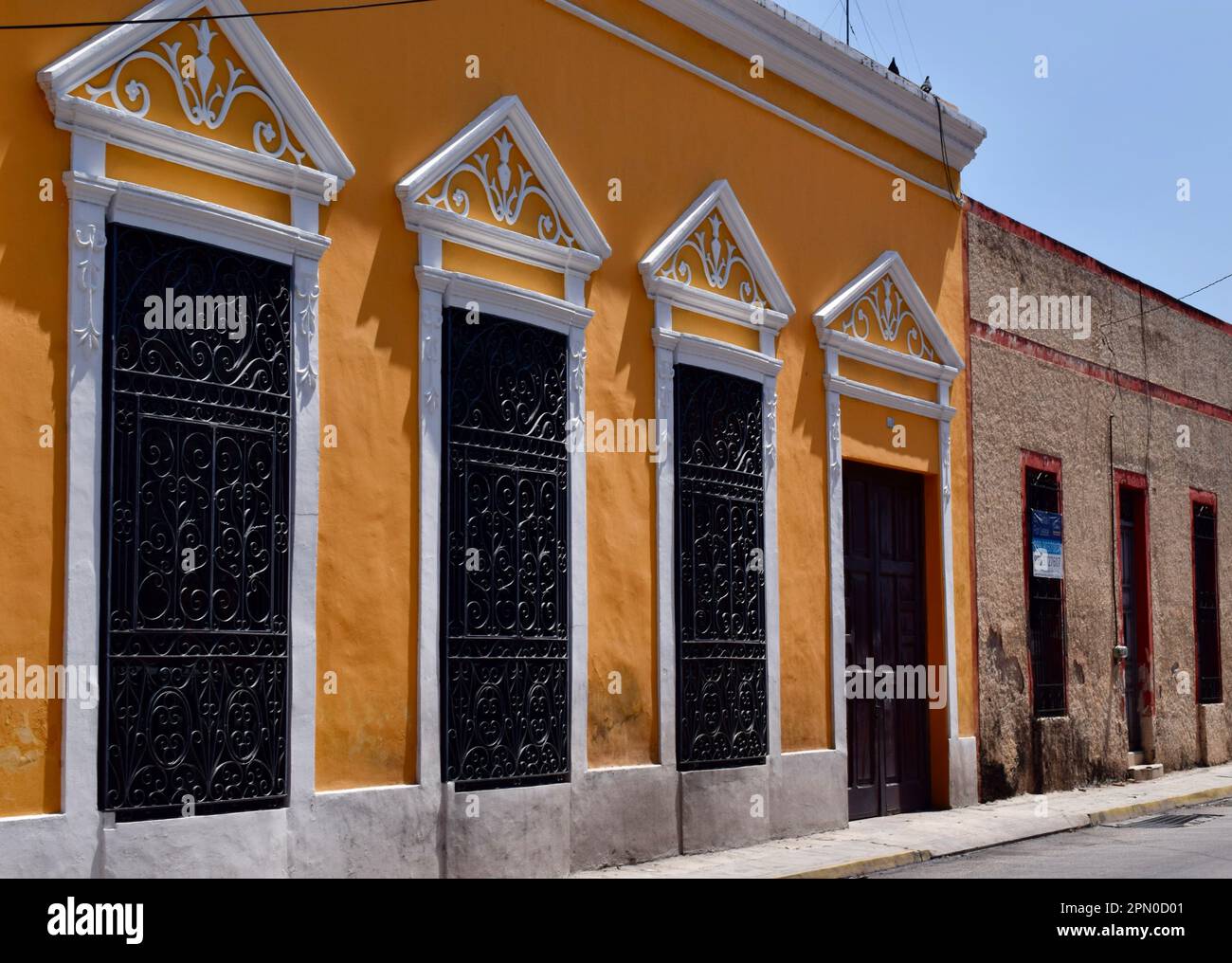 Un bâtiment colonial jaune restauré avec du fer forgé sur les fenêtres dans une rue de Merida, Yucatan, Mexique. Banque D'Images