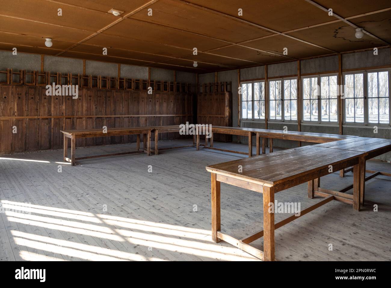 Salle commune utilisée comme salle à manger à l'intérieur des casernes du camp de concentration de Dachau avec les casiers des prisonniers le long du côté et les tabourets sur le dessus Banque D'Images