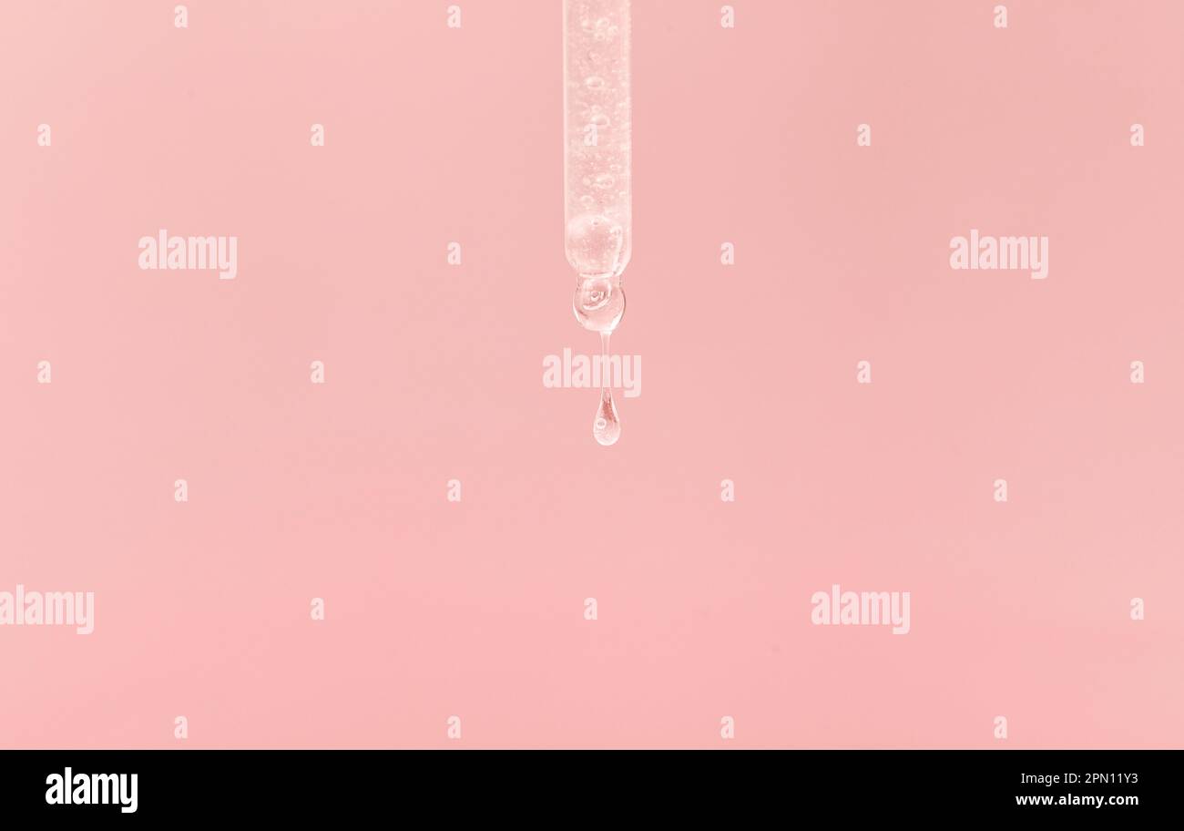 Pipette cosmétique avec une goutte transparente de sérum gros plan sur fond rose Banque D'Images