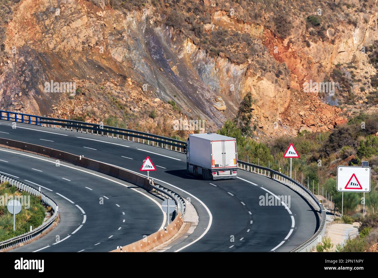 Camion avec semi-remorque réfrigérée roulant sur une route avec des panneaux d'avertissement pour vents forts. Banque D'Images