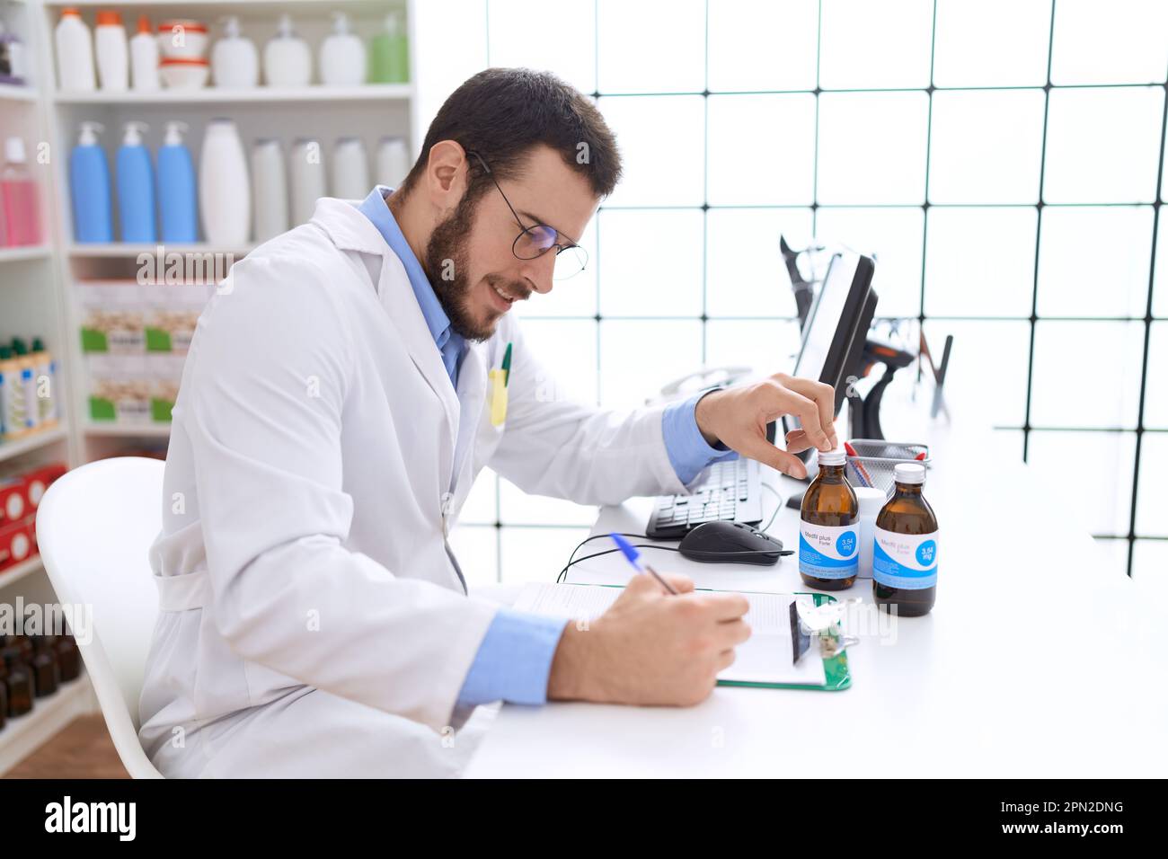 Jeune homme hispanique pharmacien tenant une bouteille de médicament écrit sur le document à la pharmacie Banque D'Images