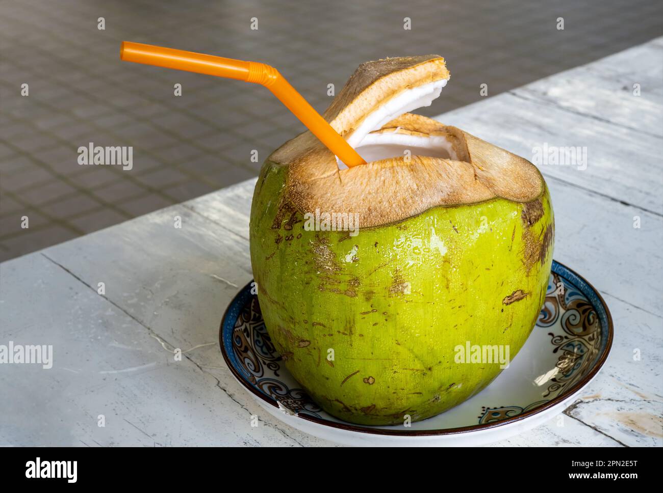 Jeune noix de coco verte fraîche avec paille à boire de couleur orange. Fruits tropicaux de noix de coco ouverts sur le dessus, montrant la jeune viande de noix de coco blanche et douce W. Banque D'Images