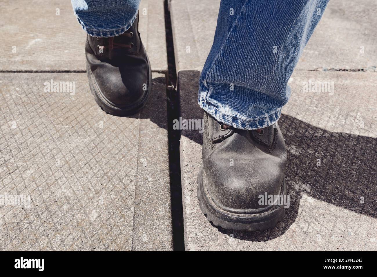 Vue détaillée de la personne portant des bottes de travail et marchant sur des blocs de béton Banque D'Images