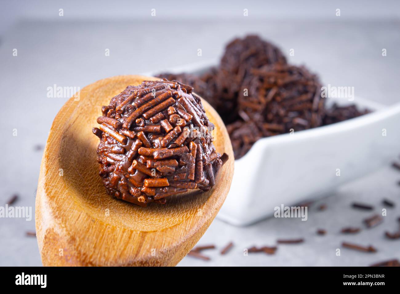 Les bonbons 'Brigadeiro' sont faits dans une cuillère en bois avec plusieurs bonbons 'brigadeiro' sur un bol blanc avec des saupoudrés de chocolat sur la table. Typique Banque D'Images