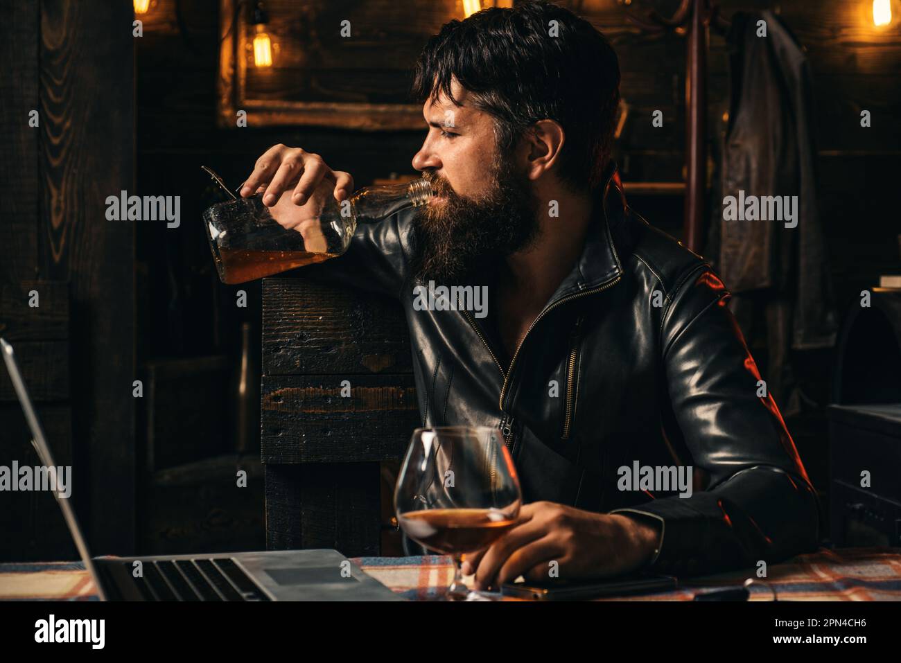 Le motard qui arrive au bar. Un homme frustré avec une barbe boit dans une bouteille de whisky. Problèmes dans les relations. Alcoolisme, alcool Banque D'Images