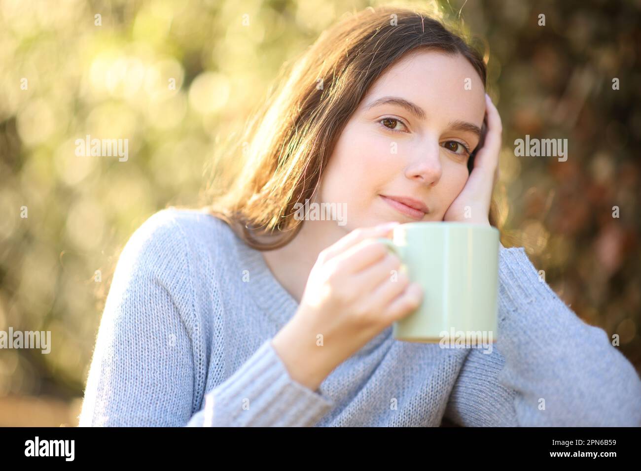 Une femme pensive assise dans un parc tenant un café vous regarde au coucher du soleil Banque D'Images