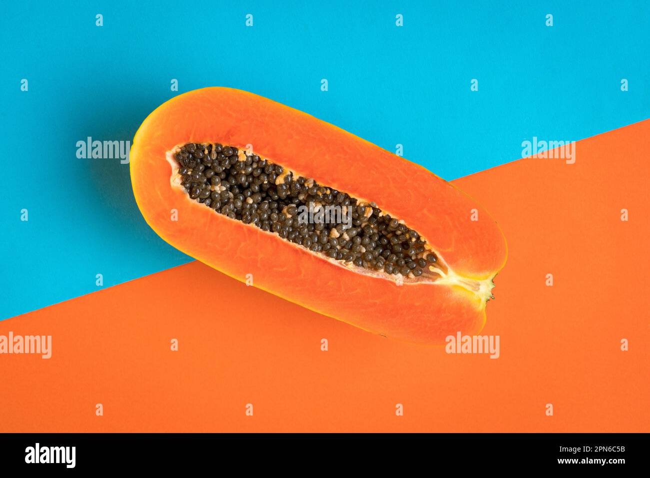 Papaye mûre coupée en deux sur fond bleu et orange. Concept d'été. Banque D'Images