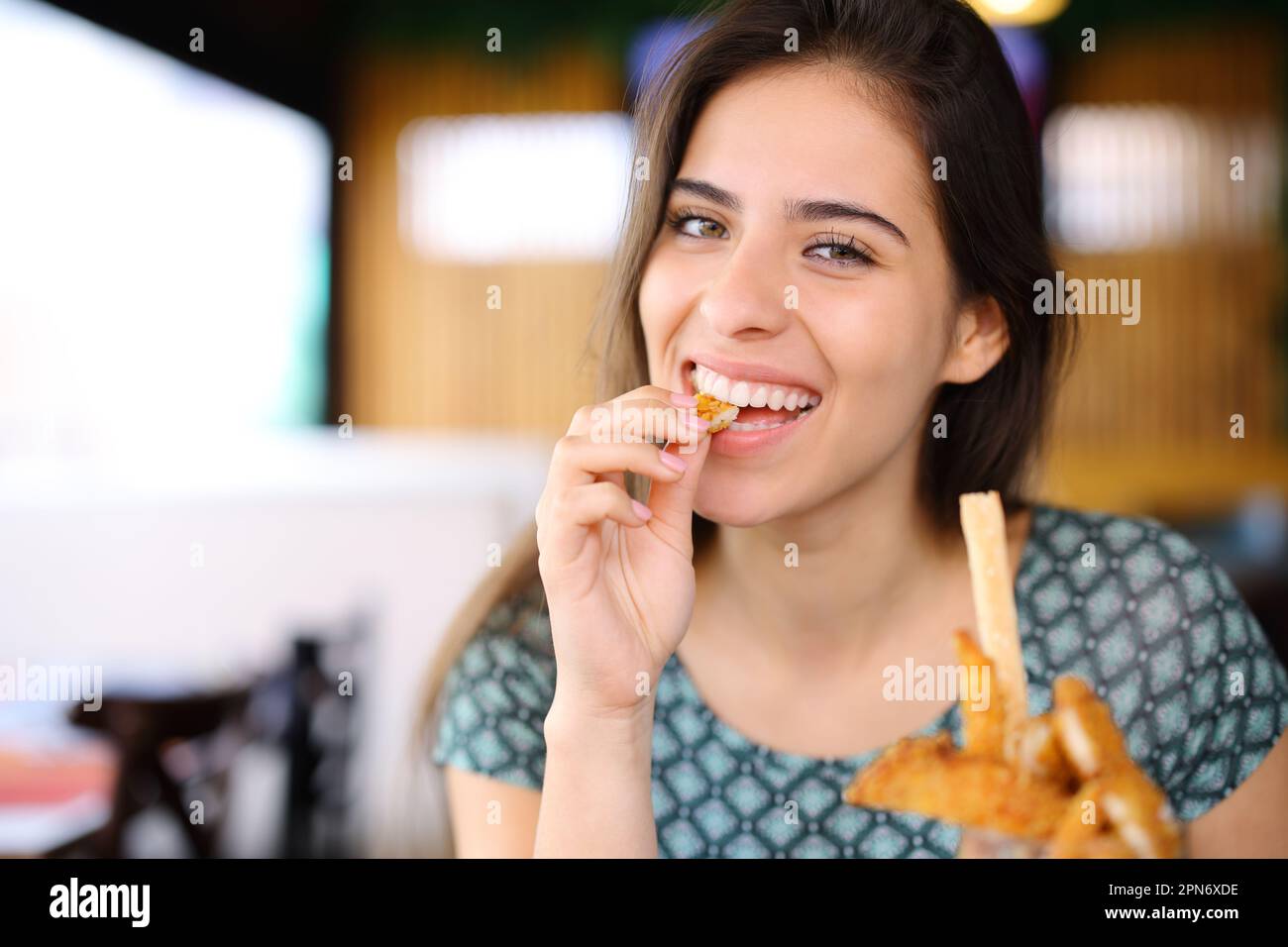 Bonne femme mangeant des doigts de poulet en regardant l'appareil photo dans un restaurant Banque D'Images