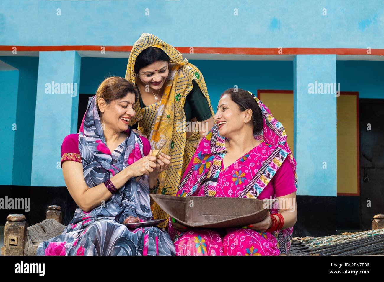 Groupe de femmes indiennes mariées traditionnelles portant sari parlant rire faire le travail à la maison ensemble à la maison en vissant la passoire de panier pour nettoyer le grai Banque D'Images
