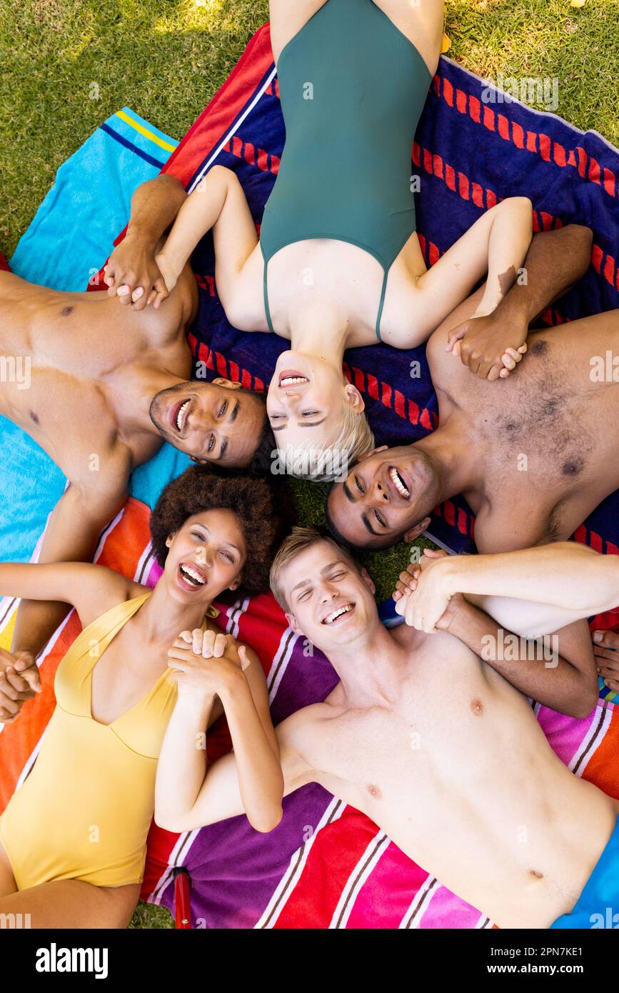 Portrait d'un groupe d'amis heureux et divers allongé sur des serviettes, tenant les mains et souriant dans le jardin Banque D'Images