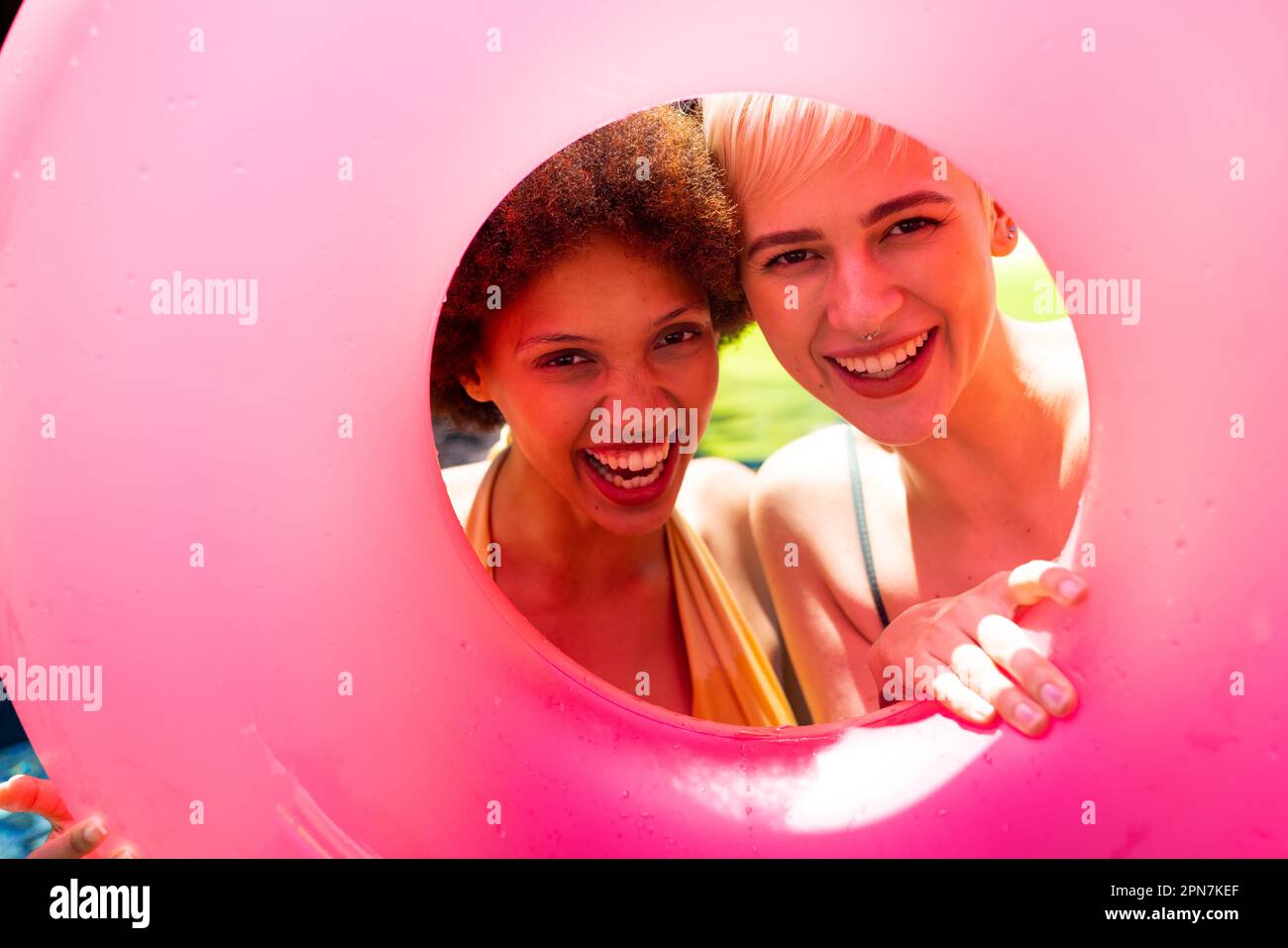 Portrait d'amis féminins heureux et variés ayant une fête au bord de la piscine, tenant un anneau de natation et souriant dans le jardin Banque D'Images