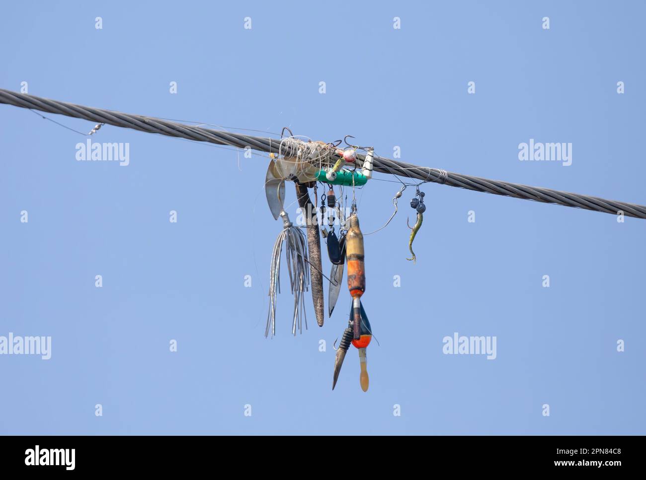 Ligne de pêche et leurres emmêlées autour de fils aériens contre un ciel bleu près d'une rivière Banque D'Images