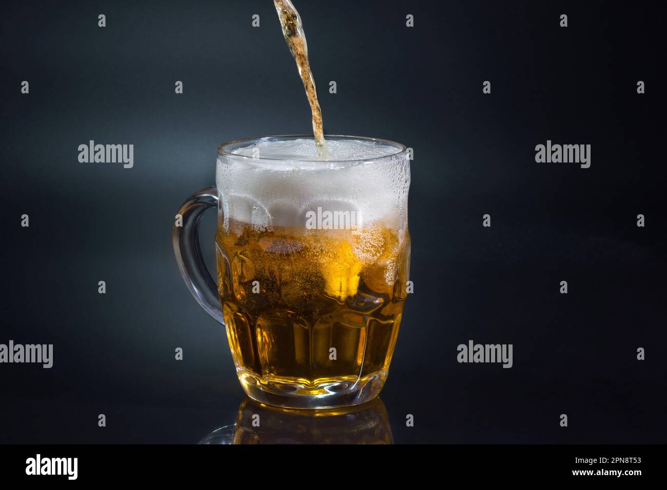 La bière coule dans le verre sur fond sombre Banque D'Images