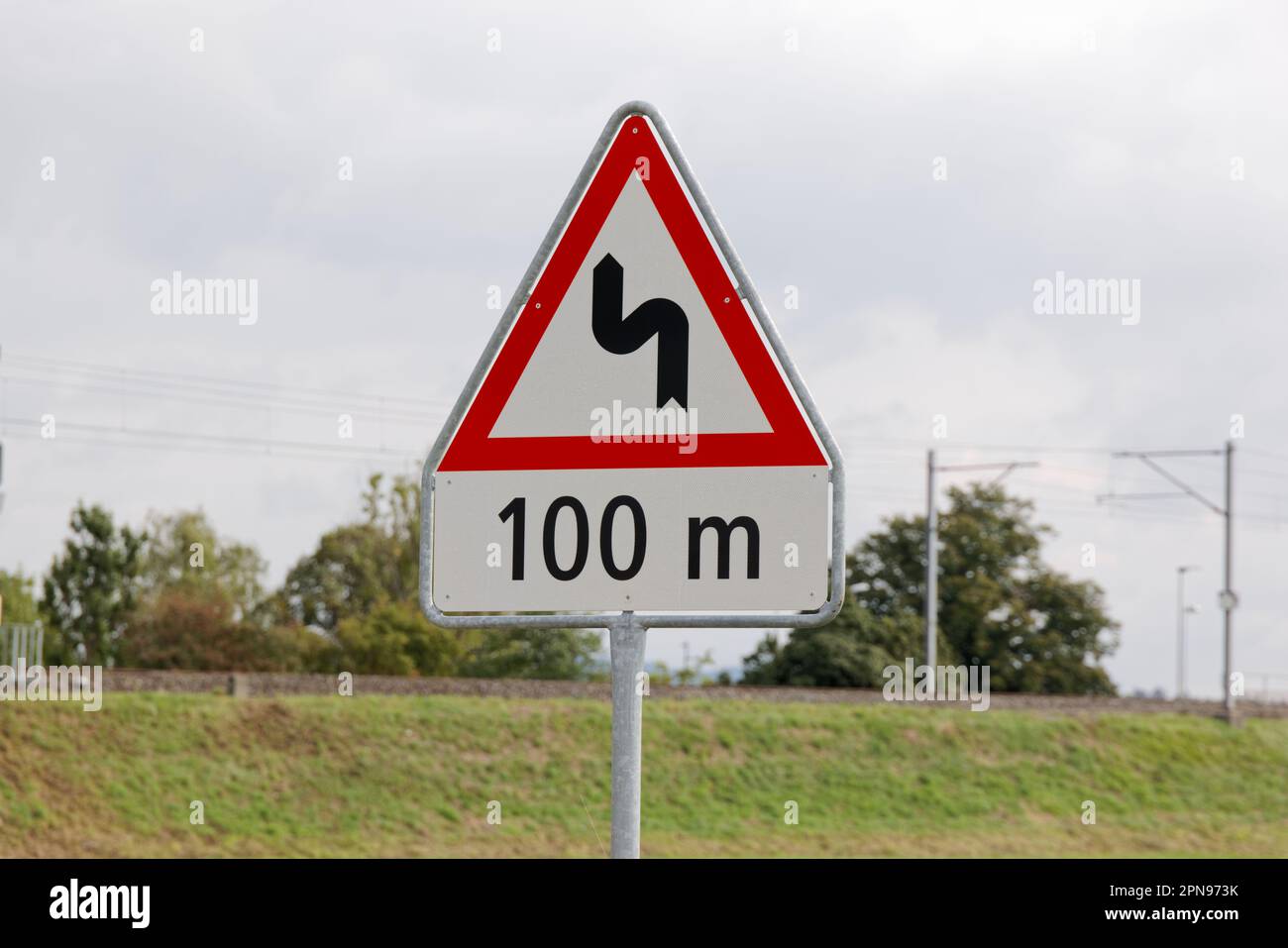 panneau de signalisation suisse : double virage à gauche. dans 100 mètres. nuageux pendant la journée sans personnes. conduire lentement peut être dangereux Banque D'Images
