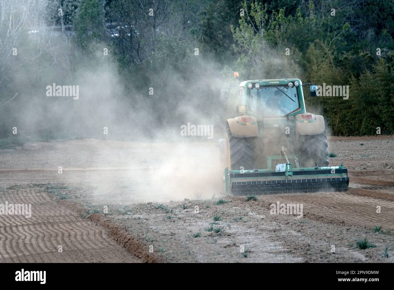 Tracteur labourant un champ couvert de poussière de sol sec de la longue sécheresse. Pianezza, Italie - avril 2023 Banque D'Images