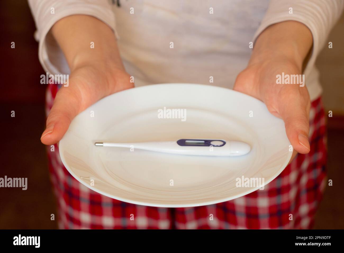 mains femelles tenant une plaque blanche avec un thermomètre électronique Banque D'Images