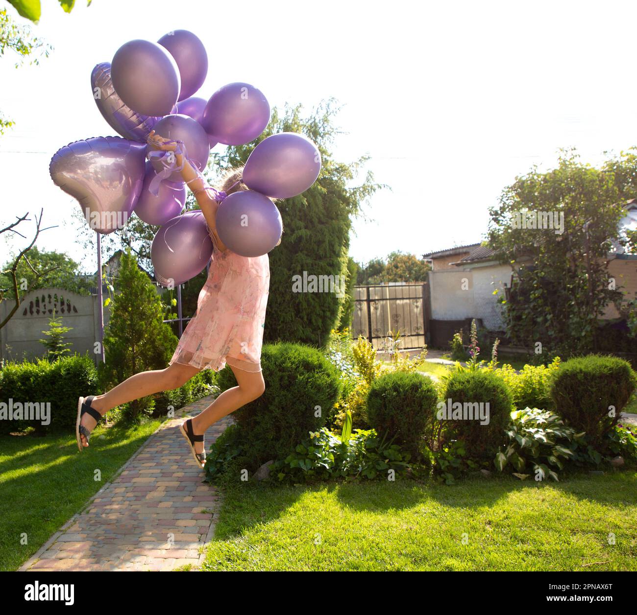 une fille méconnaissable saute en tenant beaucoup de ballons lilas dans ses mains lors d'une journée ensoleillée d'été Banque D'Images