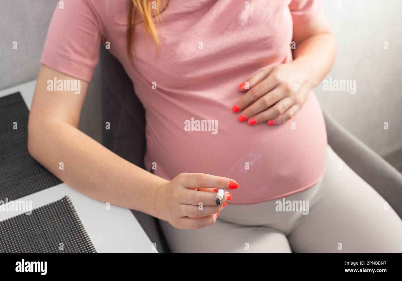 Une fille enceinte avec un gros ventre s'assoit dans la cuisine à la table et fume. Tabagisme et grossesse. Atteinte à la santé de l'enfant et de la mère, le tobac Banque D'Images