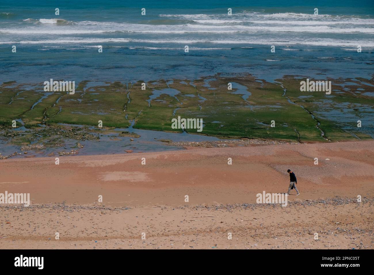Sidi Ifni, Maroc - vue aérienne d'une journée sur la promenade d'un homme sur la côte de la plage. Sable orange brun, rivage rocheux recouvert de mousse verte, vagues bleues de l'océan Atlantique. Banque D'Images