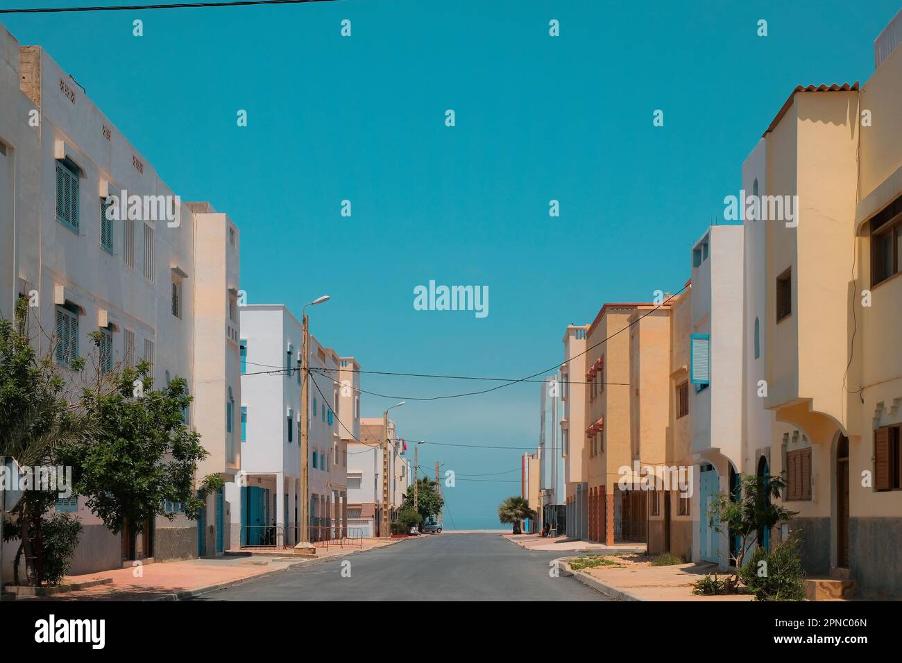 Rue vide à Sidi Ifni, Maroc bordée de bâtiments résidentiels des deux côtés. Petite ville côtière en Afrique. Jour lumineux, ciel bleu. Arrière-plan de voyage. Banque D'Images