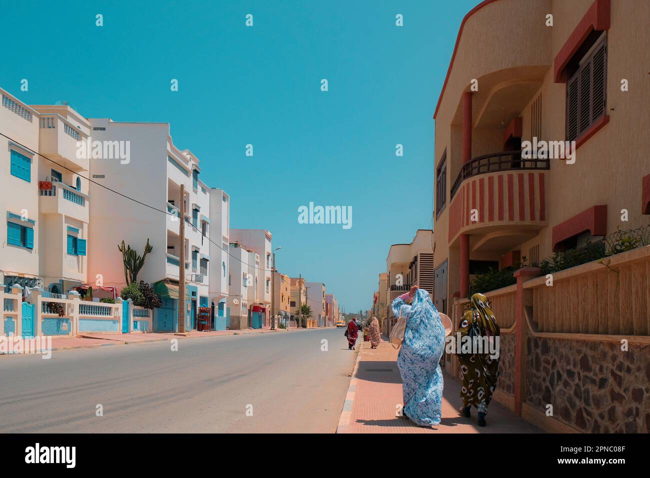 Quatre musulmanes couvertes marchent sur un trottoir à Sidi Ifni, Maroc, sur le Ramadan. Rue bordée de bâtiments résidentiels bas des deux côtés. Ville côtière. Banque D'Images