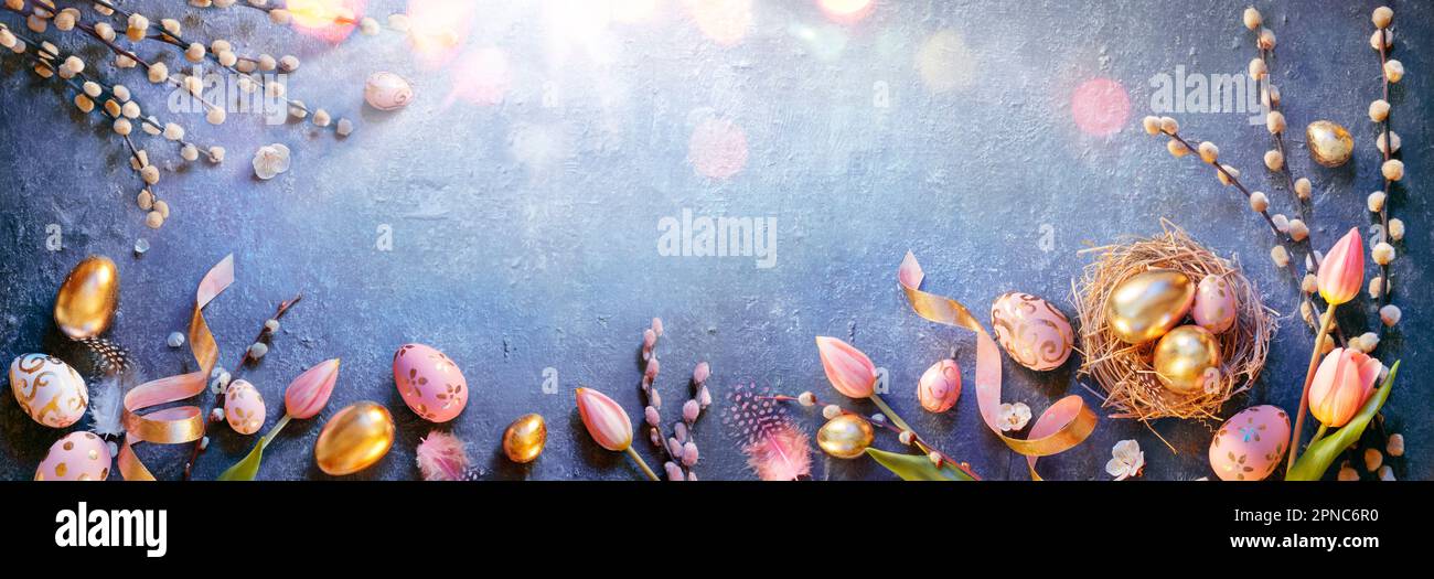 Pâques - oeufs en Nest et tulipes avec décorations dorées et roses sur table bleue avec soleil Banque D'Images