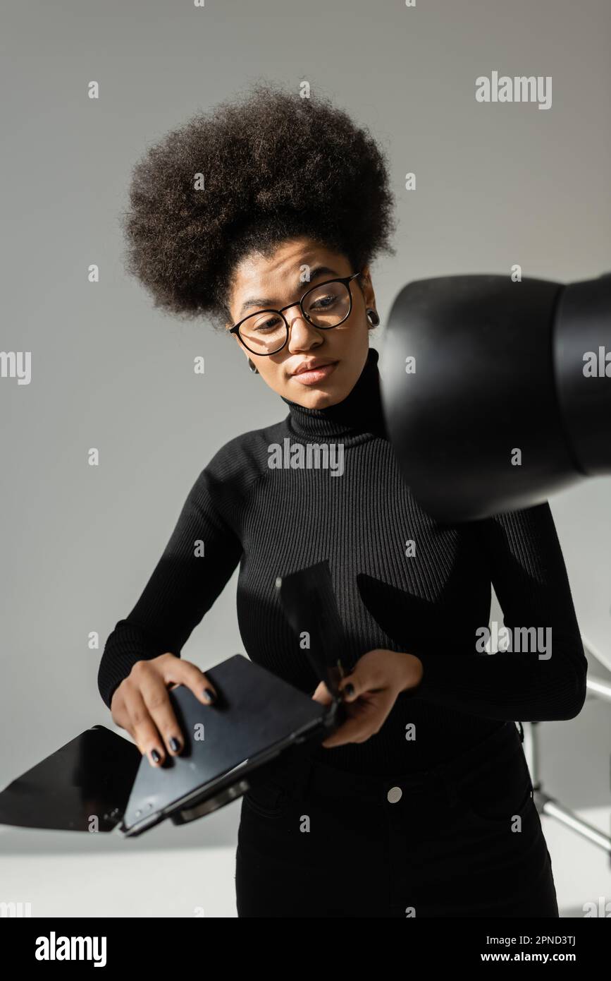 directeur de contenu afro-américain tenant une partie de la lampe stroboscopique tout en assemblant l'équipement d'éclairage dans le studio photo, image de stock Banque D'Images