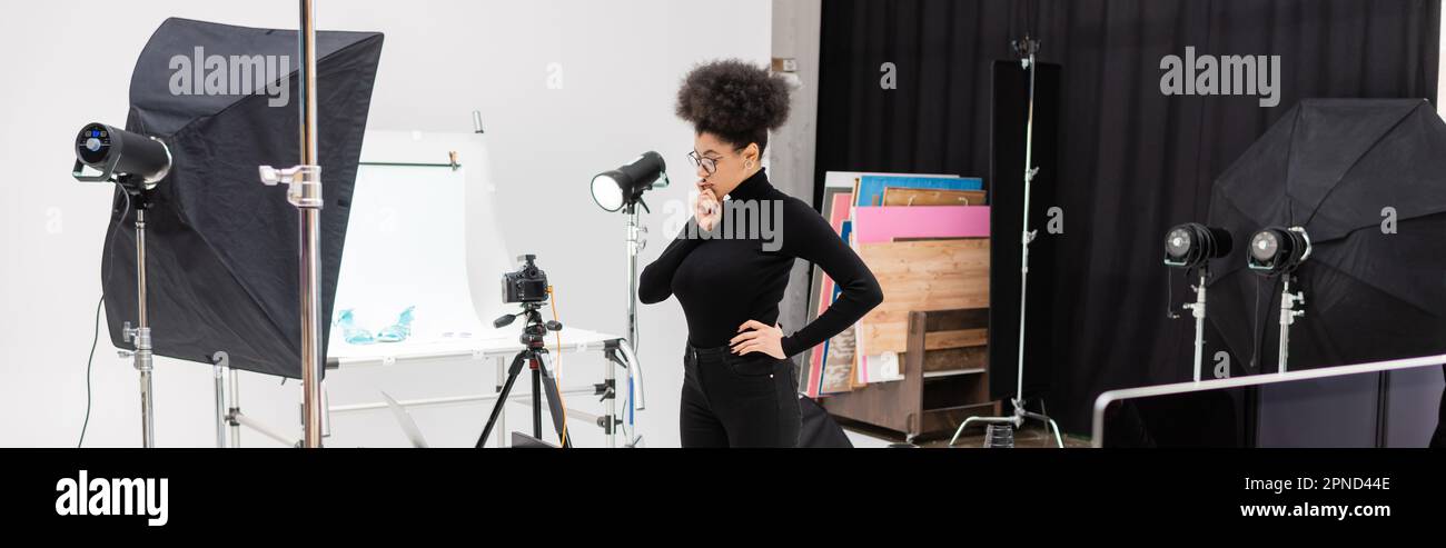 directeur de contenu afro-américain attentif, situé à proximité d'un appareil photo numérique et d'un équipement d'éclairage dans un studio photo spacieux, une bannière, une image de stock Banque D'Images