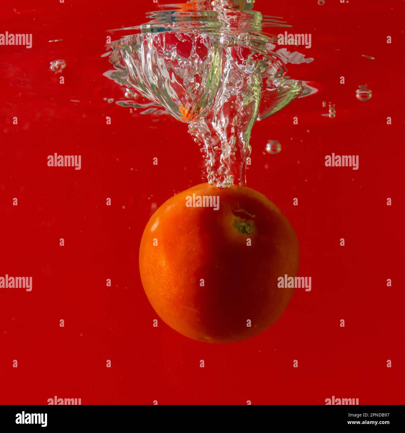 Tomate mûre tombe profondément sous l'eau avec un grand bruit. Banque D'Images