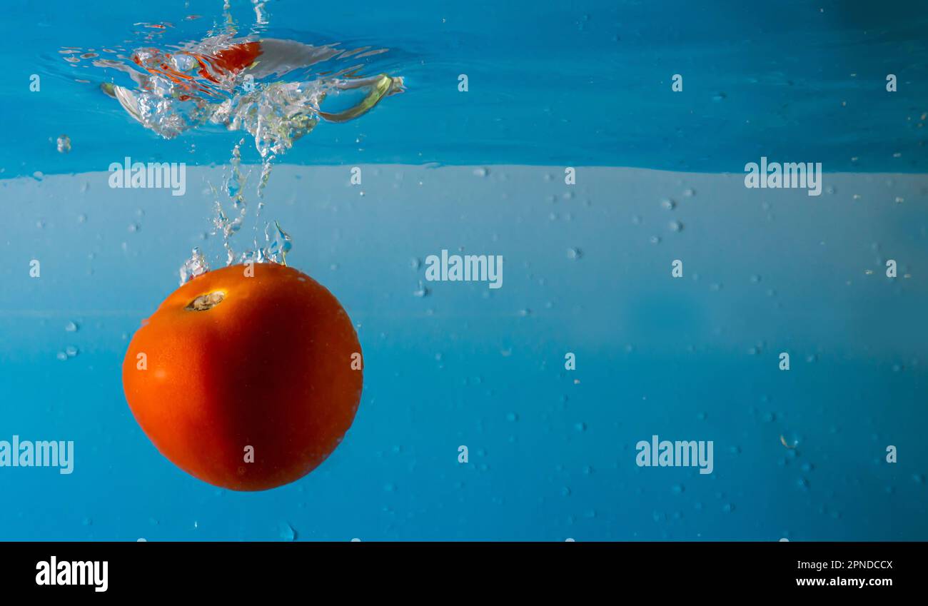 Tomate mûre tombe profondément sous l'eau avec un grand bruit. Banque D'Images