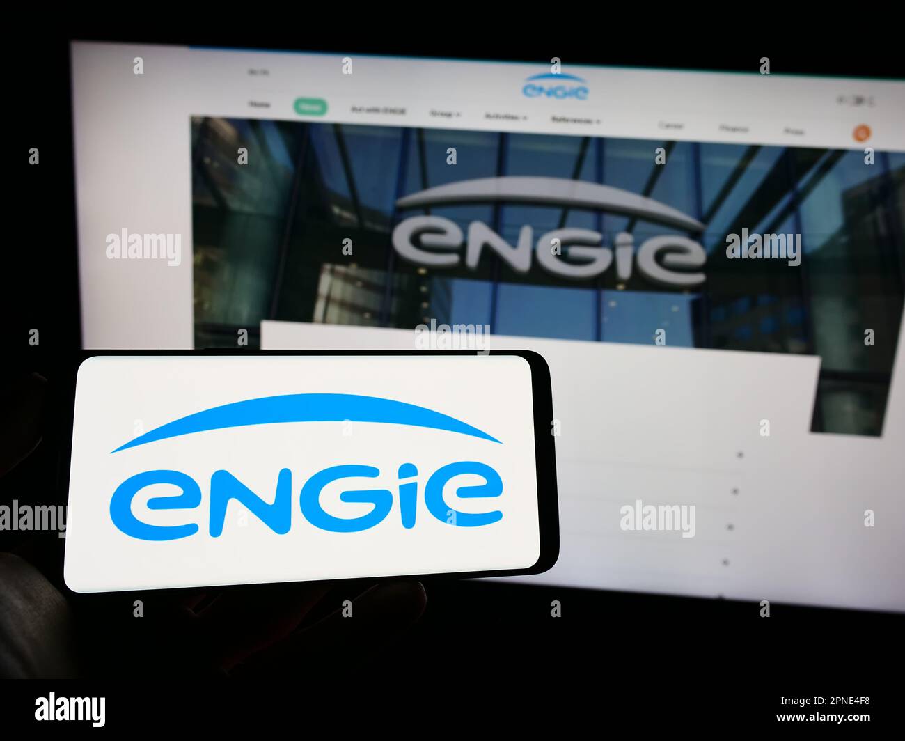 Personne tenant un téléphone portable avec le logo de la société française d'énergie Engie S.A. sur écran en face de la page web d'affaires. Mise au point sur l'affichage du téléphone. Banque D'Images