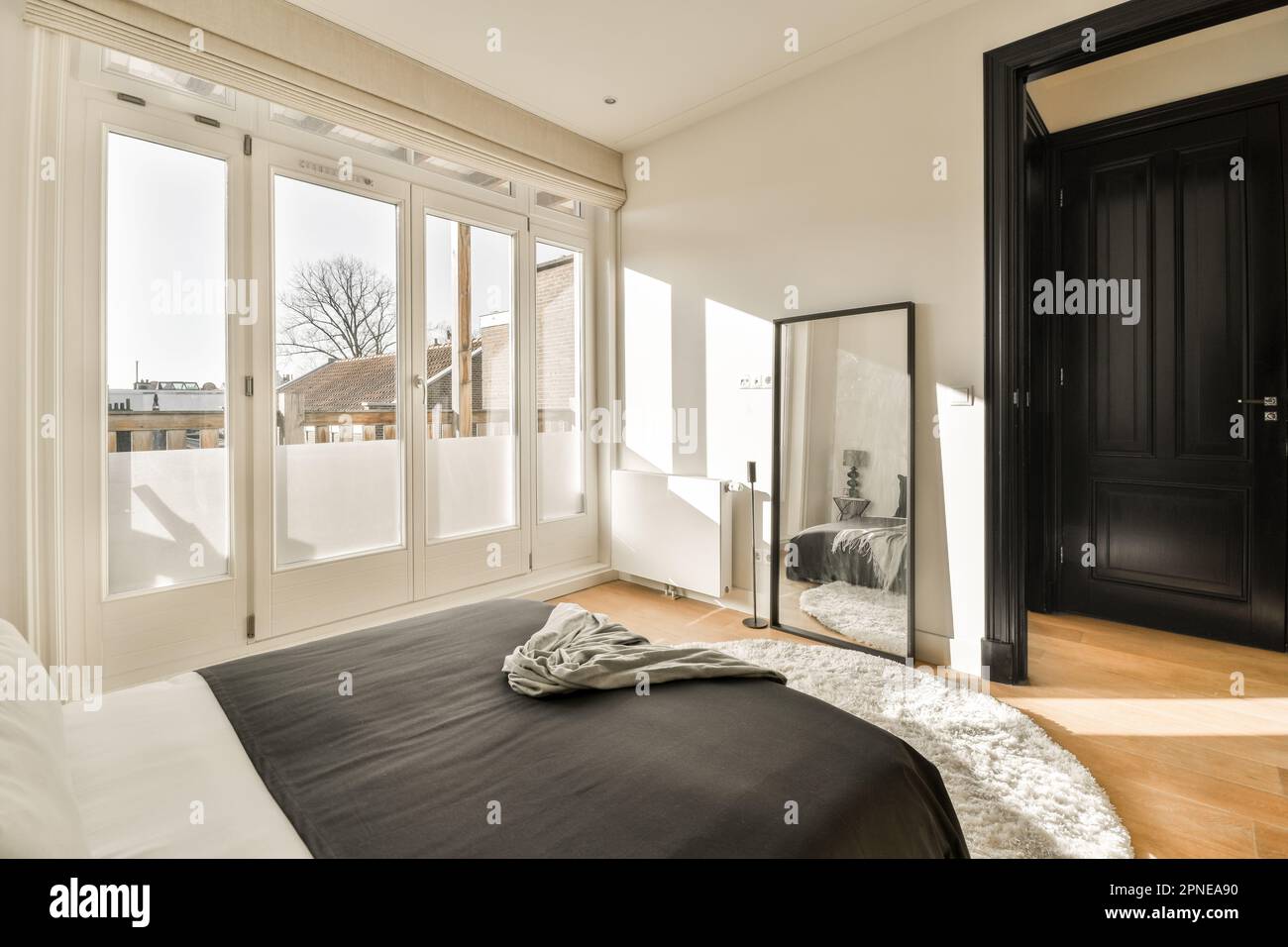 une chambre avec un lit noir et des draps blancs sur le sol, devant une grande porte coulissante en verre Banque D'Images