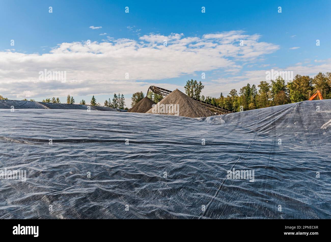 De petites collines en forme de cône à pic de saleté vidées par un tapis roulant dans une décharge active avec une grande géomembrane au premier plan. Banque D'Images