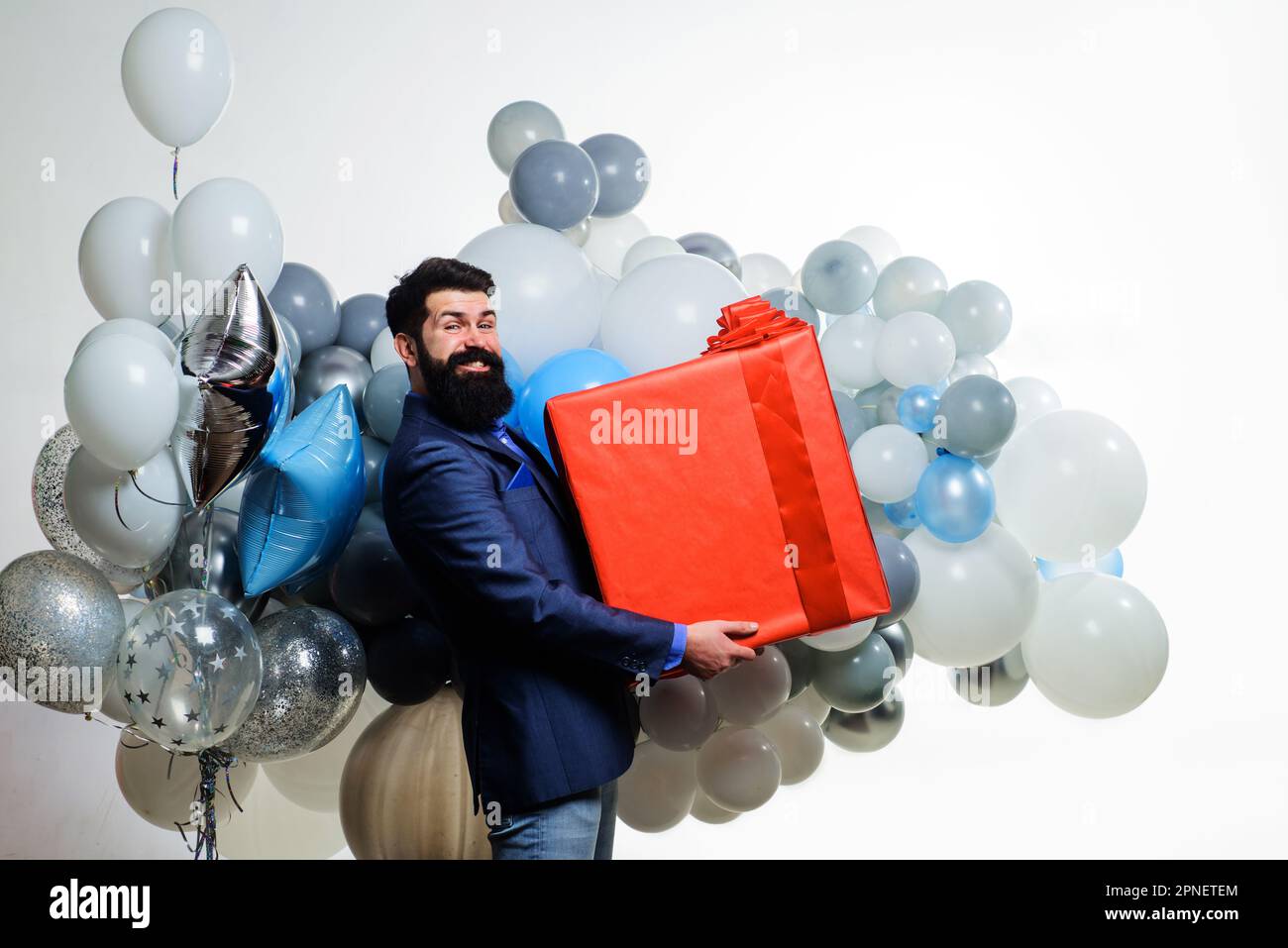 Cadeau d'anniversaire. Joyeux homme barbu avec des ballons d'hélium et une grande boîte cadeau. Fête d'anniversaire. Homme d'affaires en costume avec grand coffret cadeau. Heureux Banque D'Images