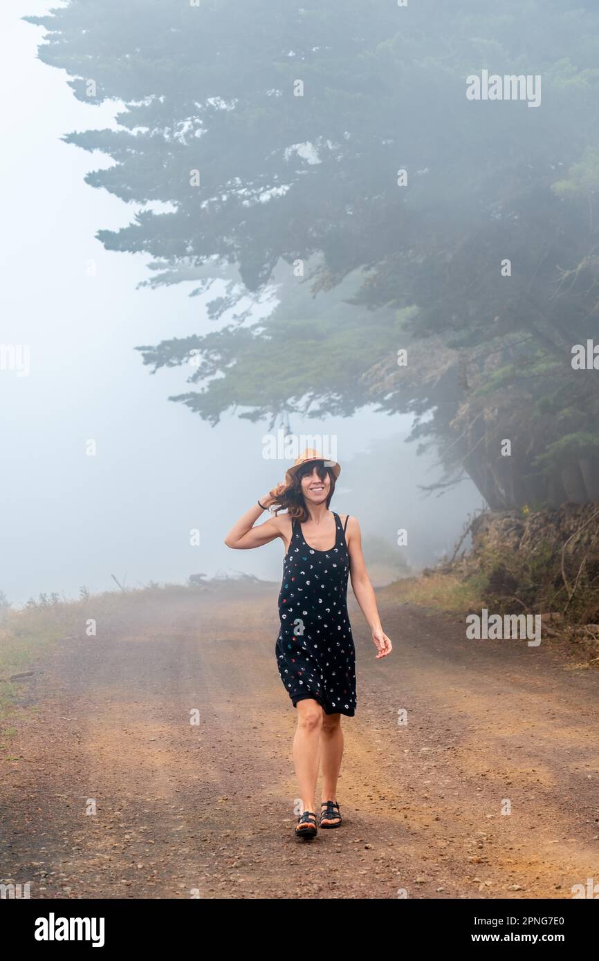 Femme touristique avec chapeau marchant à travers le chemin brumeux vers la forêt de genévrier à El Hierro. Îles Canaries Banque D'Images