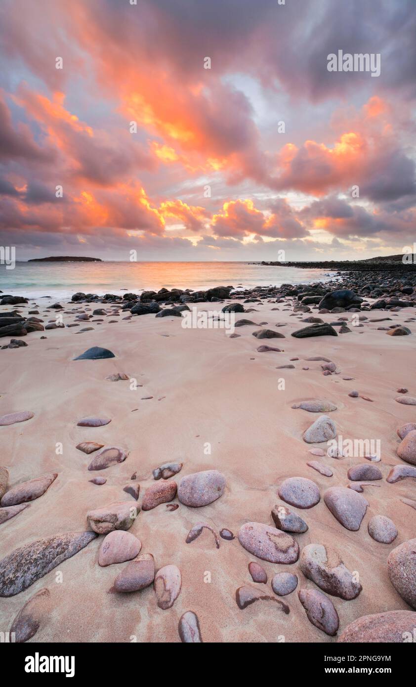 Ciel nuageux de couleur orange au coucher du soleil sur une plage de sable parsemée de pierres rondes près d'Achiltibuie sur la côte ouest de l'Écosse Banque D'Images