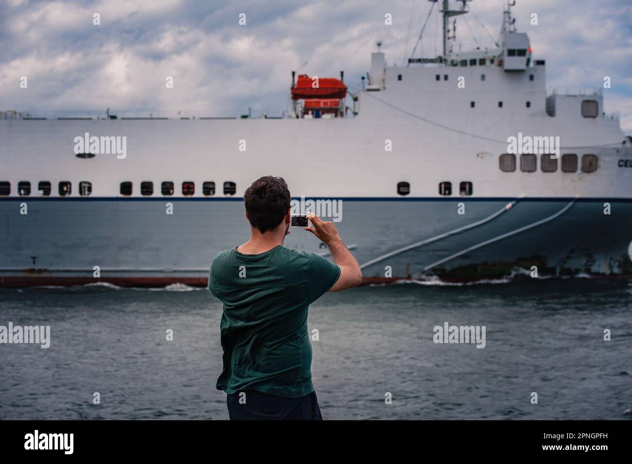 Vue arrière d'une personne qui prend une photo d'un gros navire qui passe. Être individuel ou humain faisant une photo d'un navire qui passe dans le port de Dublin Banque D'Images