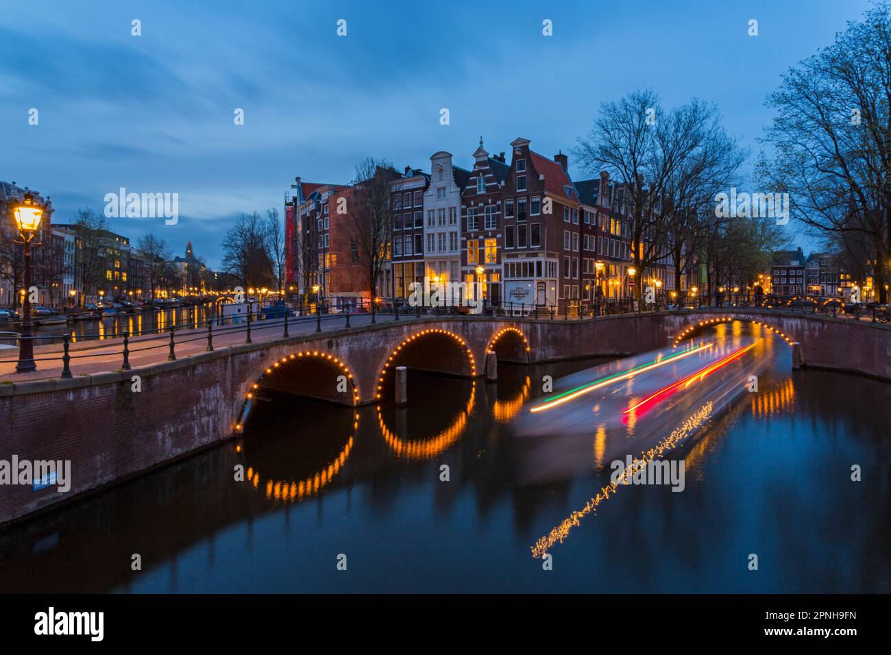 Les ponts s'illuminent à l'heure bleue du crépuscule à Amsterdam, Hollande, pays-Bas en avril - exposition longue avec des lumières de bateau passant sous le pont Banque D'Images