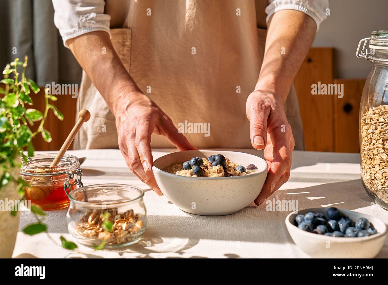 Femme préparant un petit déjeuner sain et diététique. Les mains des femmes tiennent un bol de porridge de flocons d'avoine avec des bleuets, des noix et du miel. Banque D'Images