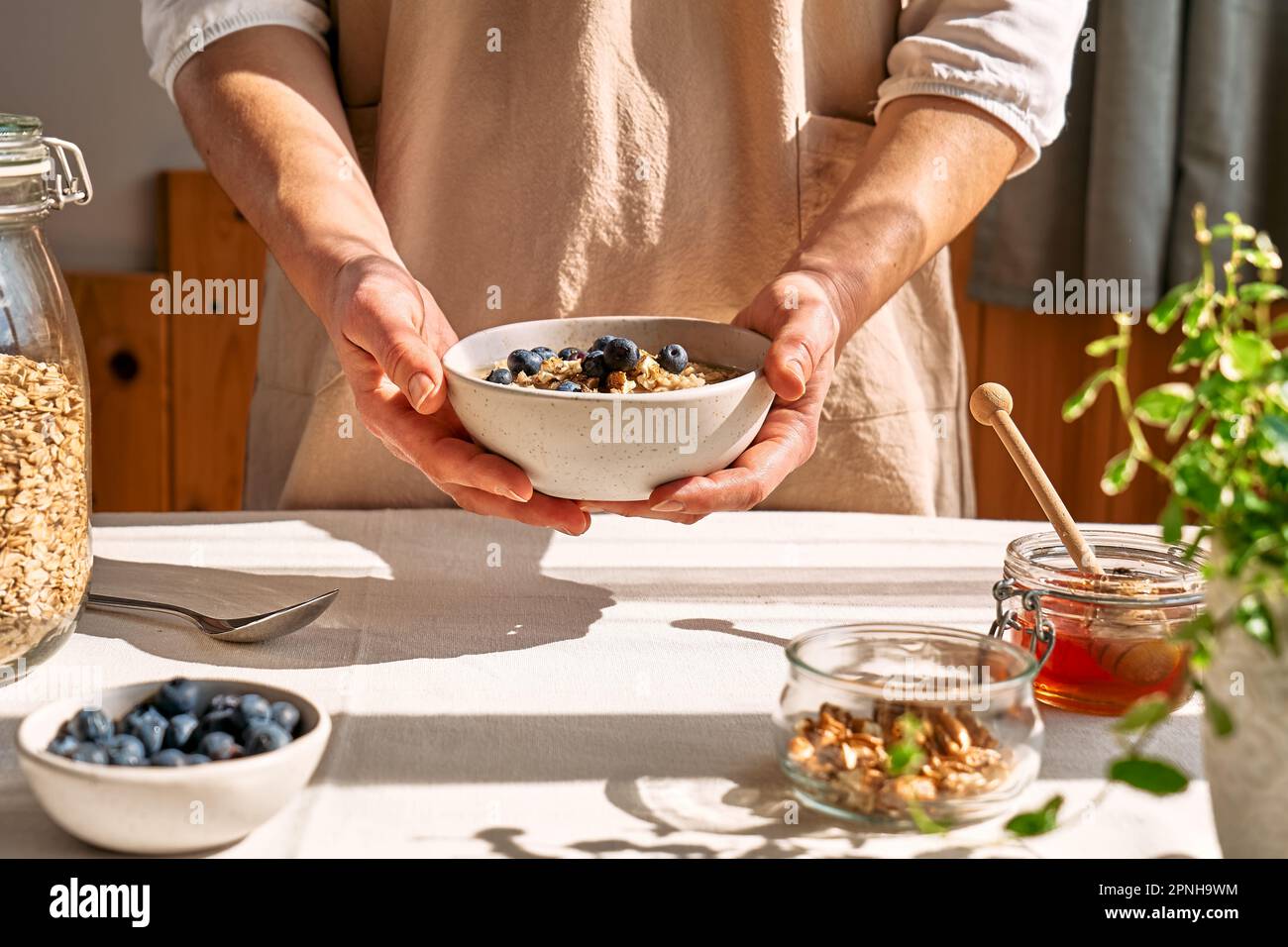 Femme préparant un petit déjeuner sain et diététique. Les mains des femmes tiennent un bol de porridge de flocons d'avoine avec des bleuets, des noix et du miel. Banque D'Images