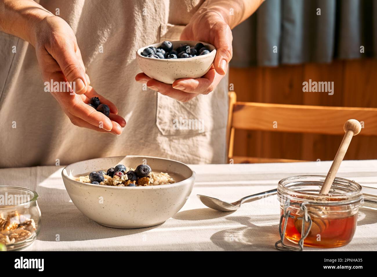 Femme préparant un petit déjeuner sain et diététique. Femelle mettant à la main des myrtilles dans le bol avec porridge de flocons d'avoine avec des noix et du miel. Banque D'Images