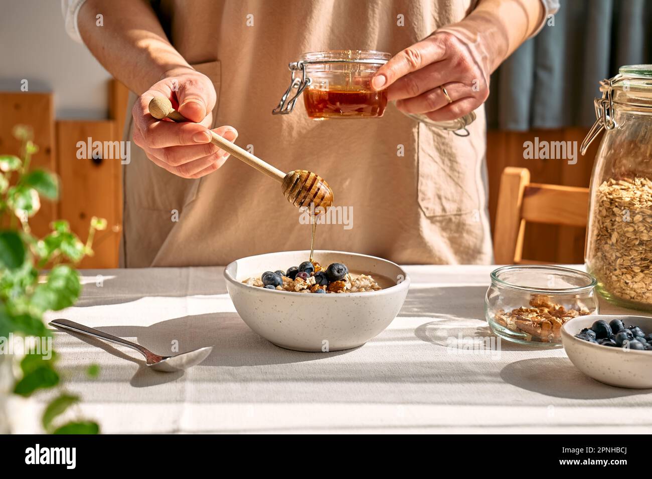 Femme préparant un petit déjeuner sain et diététique. Une femelle verse le miel à la main dans le bol avec du porridge de flocons d'avoine, des noix et des myrtilles. Banque D'Images