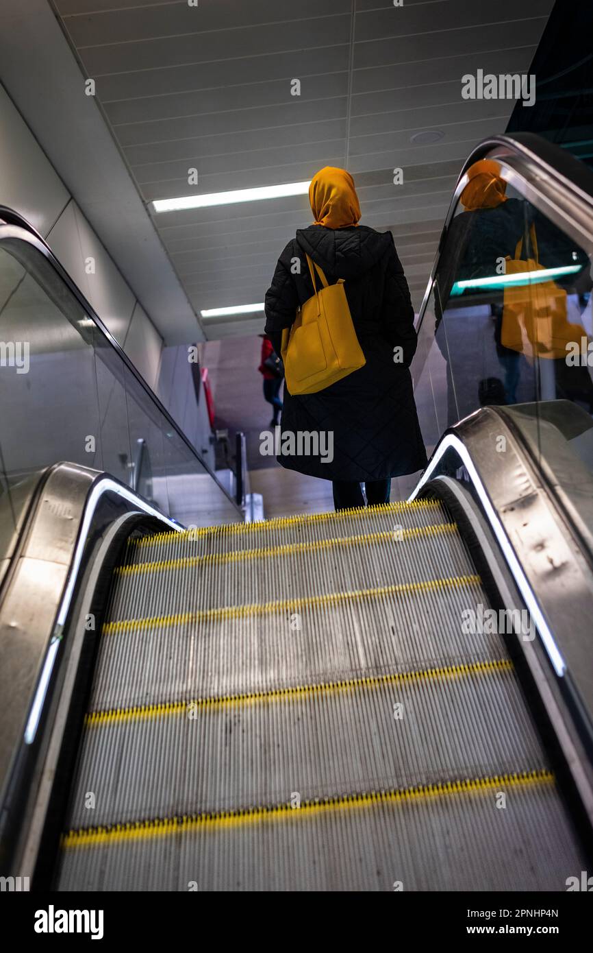 Femme descendant un escalator avec un sac sur son épaule portant un foulard Banque D'Images